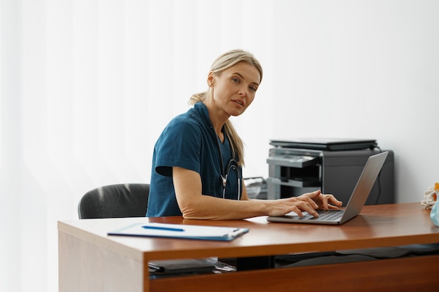 Female healthcare worker doing some paperwork and using laptop while working at doctors office