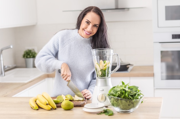 Female on a healthy diet chopping fruits to a blender for a raw food mixed snack.