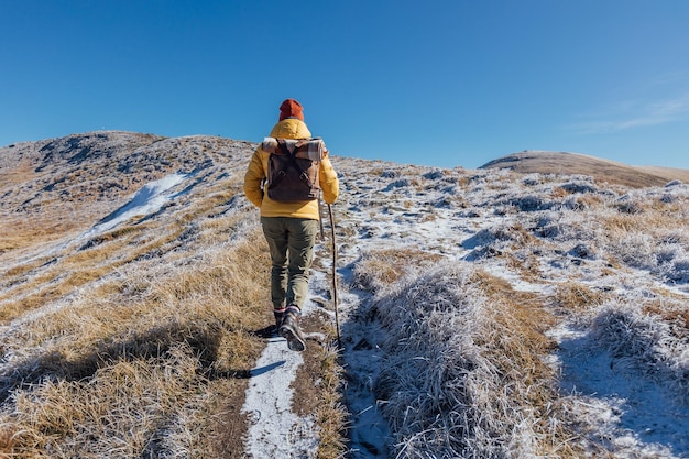 Female hiker climbing a snowy mountain range hill against mountains and clear blue sky