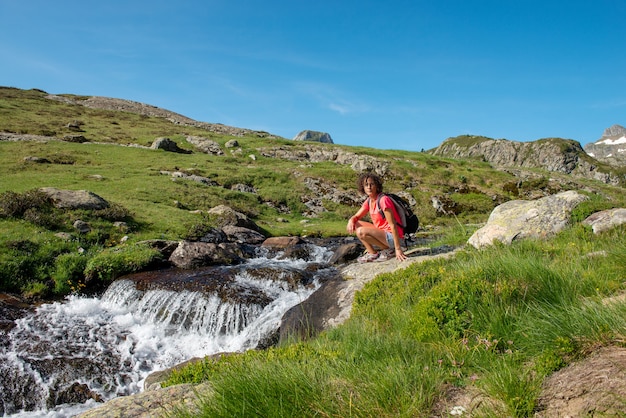 Female hiker crouch near wild splashing waterfall