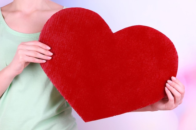 Female holding big red heart on bright background