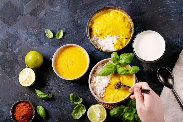 Female holding ceramic bowl of yellow curry served with basil and limes