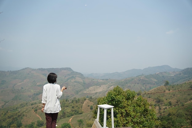 Behind of female holding hot coffee and looking at mountains view in the morning.