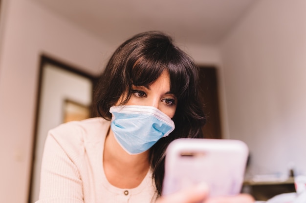 Female at home in breathing medical respiratory mask on her face using mobile phone. pandemic coronavirus, virus covid-19. Quarantine, prevent infection concept. Focus on her face.