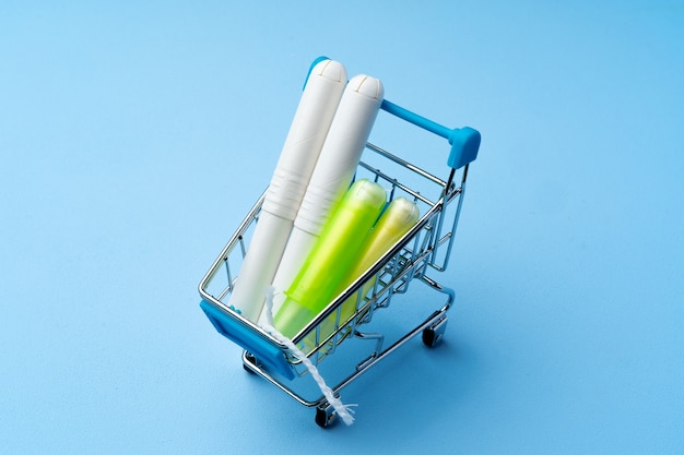 Female hygienic tampons in shopping trolley on blue close up