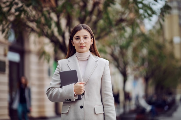 Female influencer standing on the street and holding tablet in hands. Millennials and their social life.