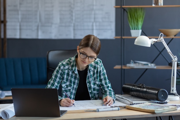 Female interior designer working in office with laptop architect thinks over architectural plan sear...