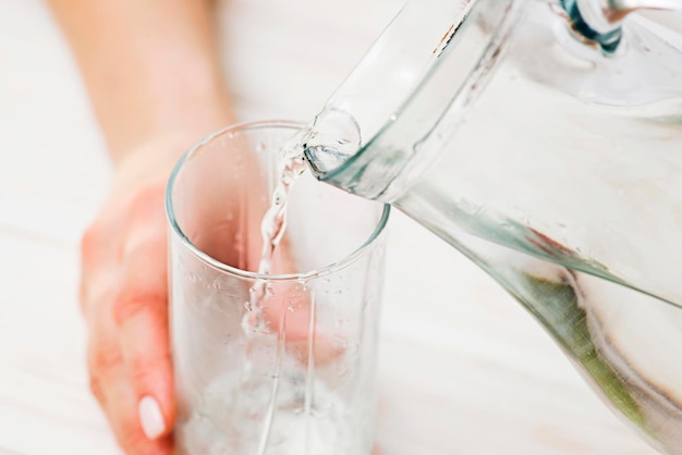 A female is pouring fresh clear water from a jug into a glass