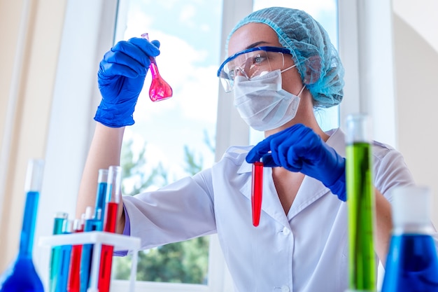 Female laboratory assistant conducts clinical laboratory research with various scientific glassware and tubes for test. Medicine, pharmacy and cosmetology concept.