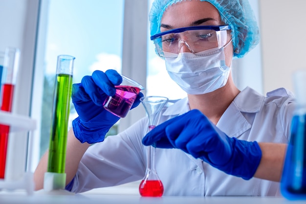 Female laboratory assistant using various scientific glassware and test tubes for clinical laboratory researches and tests. Medicine, pharmacy and cosmetology concept.