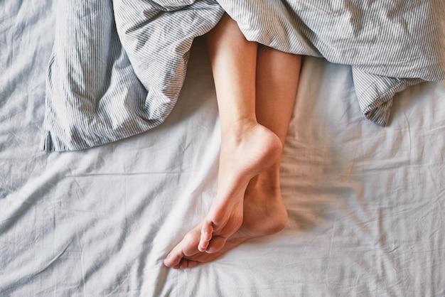 Female legs in the bed under blanket