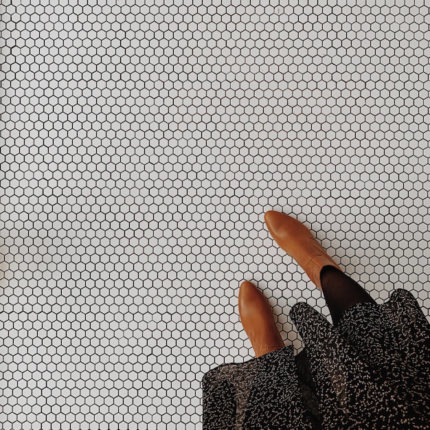 Female legs feet on white mosaic tile floor background Minimal aesthetic fashion concept with leather boots and skirt Top view