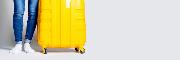 Female legs in jeans and a yellow suitcase on a light background. Banner