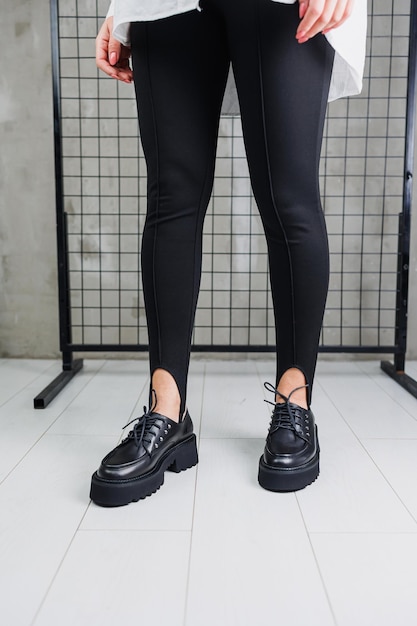 Female legs in trendy black leggings and loafers laces on leather shoes details of a stylish autumn fashion look