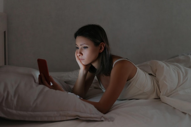 Female lying in bed and looking at her smartphone at night