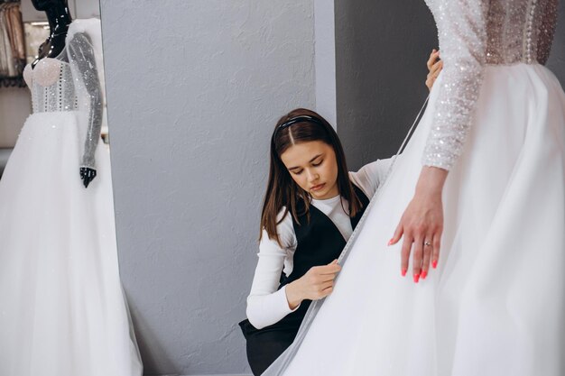 Female making adjustment to wedding gown in fashion designer studio Bride wearing her wedding gown with female dress designer making final adjustments on dress