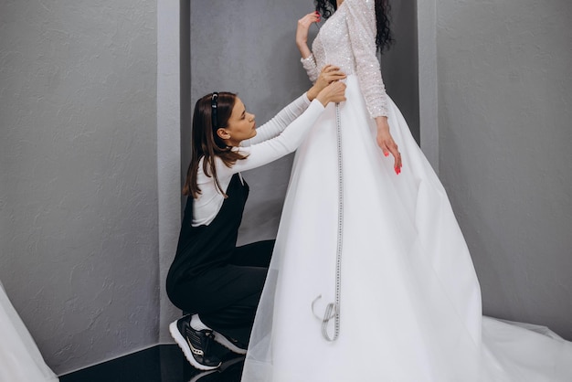 Female making adjustment to wedding gown in fashion designer studio Bride wearing her wedding gown with female dress designer making final adjustments on dress