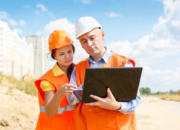 Female and male construction workers looking at laptop of houses under construction