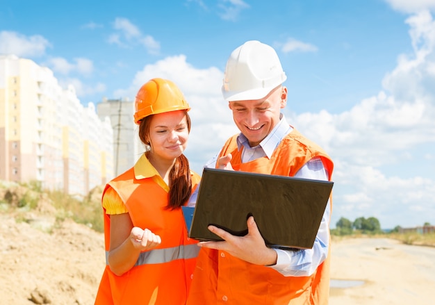 Female and male construction workers looking at laptop of houses under construction