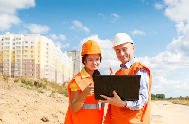 Female and male construction workers looking at laptop of houses under construction