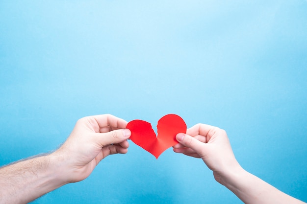 Female and male hand break a paper red heart on a blue