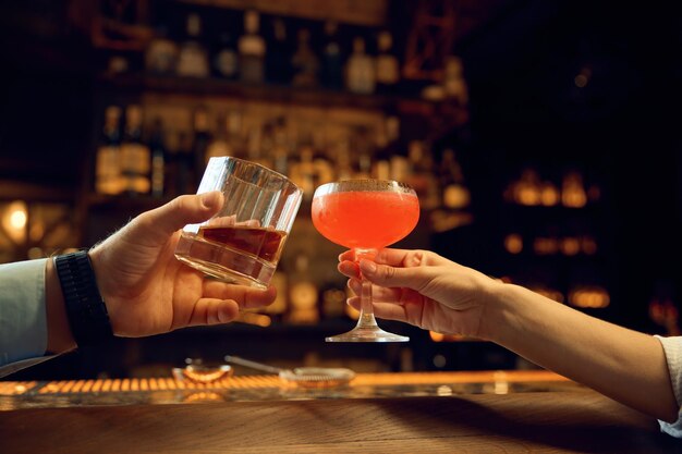 Photo female and male hands clinking glasses with alcoholic drinks closeup