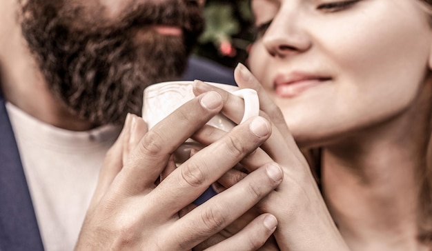 Female and man hands holding cup of coffee Lovely couple holding cup of coffe in hands Bearded man hugs girl