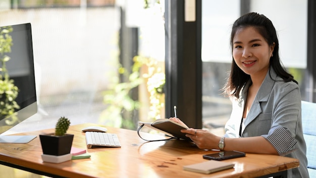 Female manager making a notes on her notebook sitting at her desk and working on computer