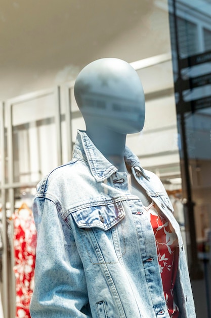 Female mannequin in a denim jacket in a glass showcase of a clothing store Fashion style and beauty Closeup Vertical