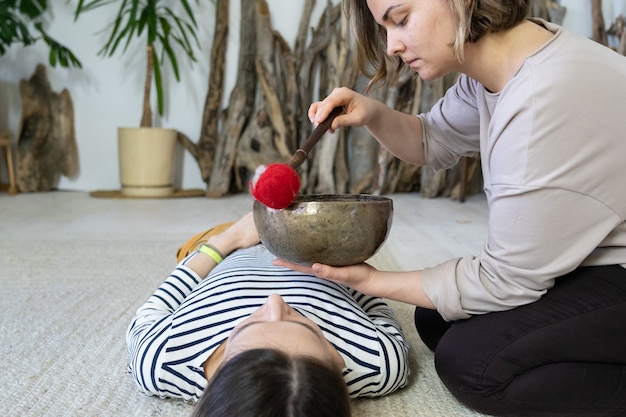 Photo female masseuse perform traditional tibetan sound therapy singing bowls massage at relaxed woman