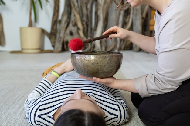 Photo female masseuse perform traditional tibetan sound therapy singing bowls massage at relaxed woman