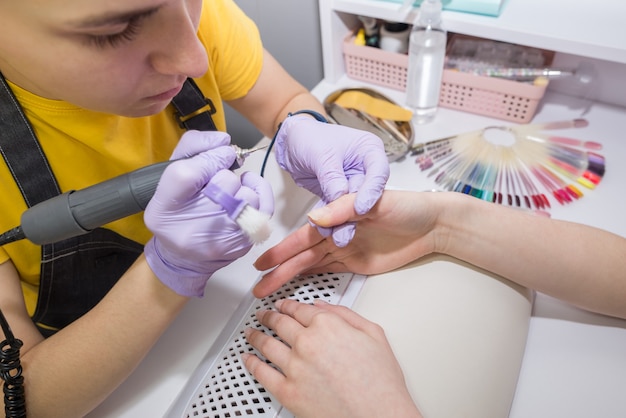 A female master uses an electric cuticle machine during a manicure at a salon. Hardware manicure close-up. Hand care concept.