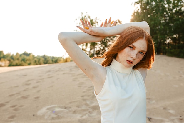 female model with long ginger hair and in white summer dress looking at camera