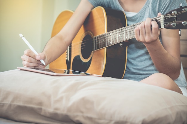 Female musicians play guitar and write songs using the tablet.