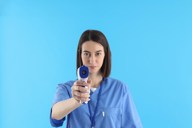 Female nurse with thermometer gun on blue background