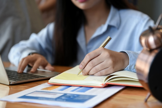 Female office workers using laptop and writing notes.