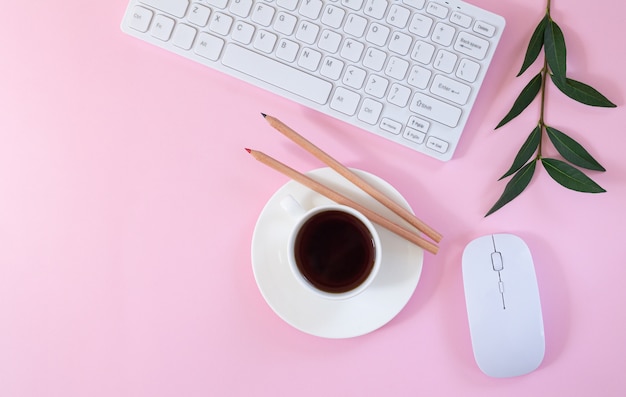 Female office workplace with keyboard, computer mouse, cup of coffee and plant on pink background. Flat lay, top view