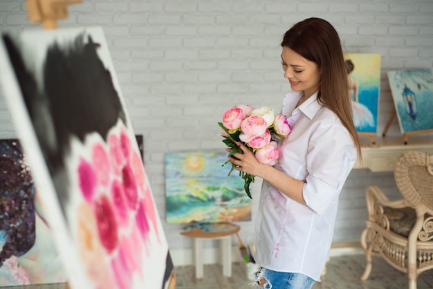 Female painter drawing in art studio using easel. Portrait of a young woman painting with oil paints, side view portrait