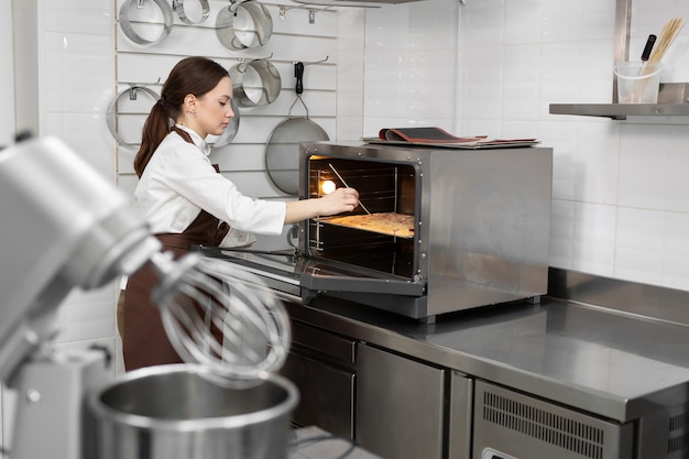 Photo female pastry chef puts the sponge dough in the oven and checks the dough with a wooden stick