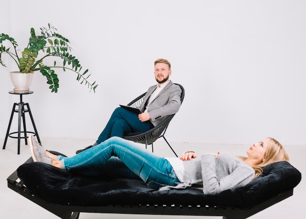 Female patient lying on couch in front of her contemplated psychologist in the clinic