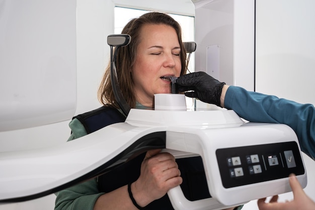 A female patient stands still in dental Xray machine to create a detailed image teeth