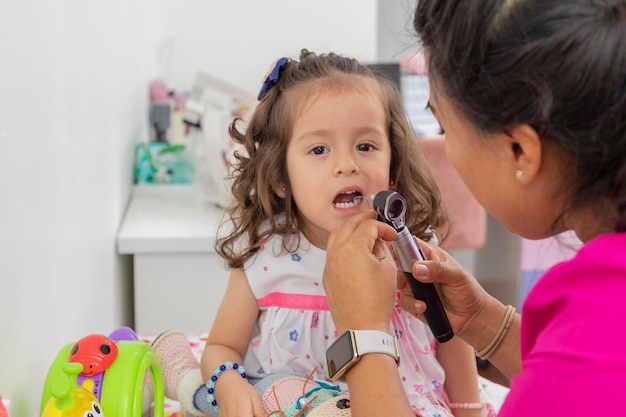 Female pediatrician doctor checks a little girl's mouth with a wooden spatula