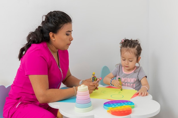 Female pediatrician doctor drawing with a little girl in her office Pediatrician woman giving consultation to a little girl