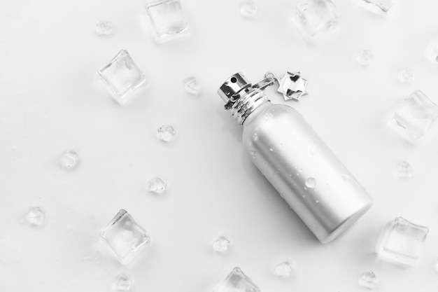 Female perfume silvery bottle Objective photograph of metallic perfume bottle in ice cubes and water on white table View from above Mockup product photo concept of freshness