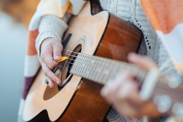 Female person playing guitar with the help of mediator near the water in nature Practicing playing the instrument on the fresh air on a cool autumn evening