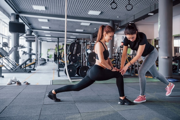 Female personal trainer helping woman doing exercises in the gym.