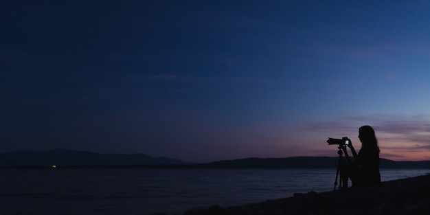 Female photographer taking photos on the beach at dusk