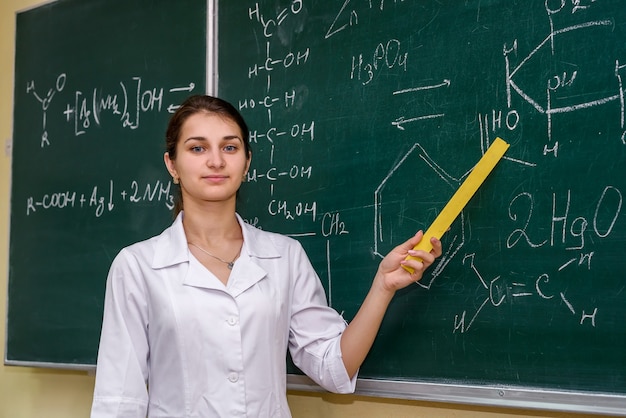 Female portrait. Chemistry teacher standing near class board pointing on it