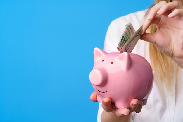 Female putting money into pink piggy bank against blue background