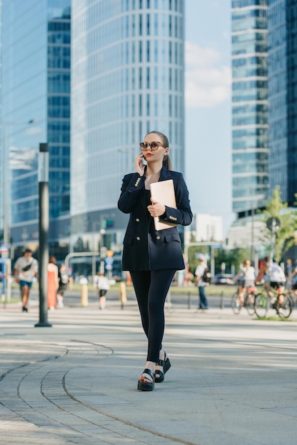 Female realtor in a blazer is strolling with a laptop in the financial district